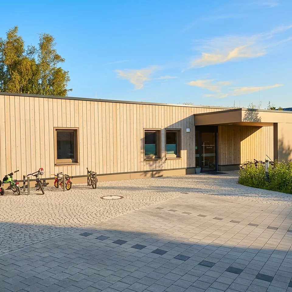 Moderner, eingeschossiger Kindergarten mit leerem gepflastertem Hof und mehreren abgestellten Kinderfahrrädern unter blauem Himmel.